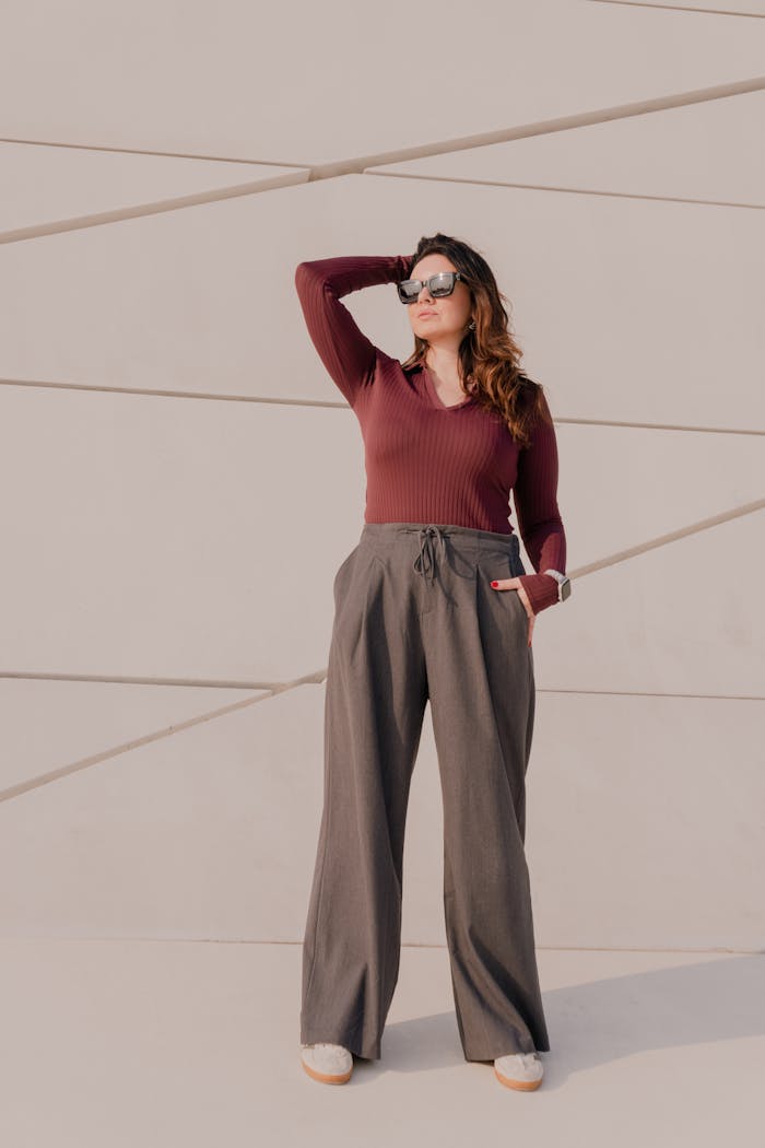 Stylish woman posing confidently outdoors against a modern architectural backdrop, wearing casual chic attire.