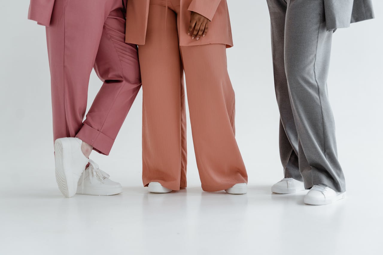 Three people wearing stylish wide-leg pants and white sneakers on a white background. Studio shot.